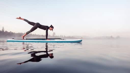 Anlagechance in turbulenten Märkten Woman practicing paddle board yoga on lake Kirchsee in the morning, Bad Toelz, Bavaria, Germany