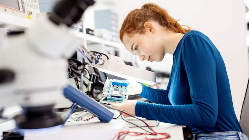 Top-Pick-Schweiz-Portfolio Eine Frau untersucht in einem Labor konzentriert eine elektronische Leiterplatte unter einer Arbeitslampe