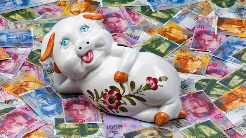Mit wenig Geld trotzdem Investieren - so geht's Ein Sparschwein liegt auf Schweizer Banknoten.