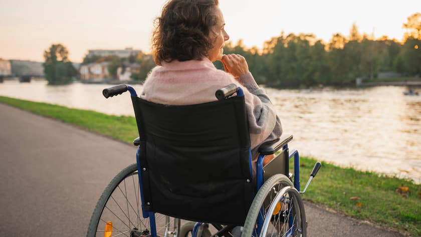 Finanzielle Gefahren bei langer Krankheit - und wie sie sich eindämmen lassen Eine ältere Frau sitzt im Rollstuhl und blickt auf den Fluss.